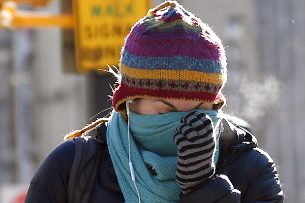 A person in hat, scarf and gloves bracing against the cold wind