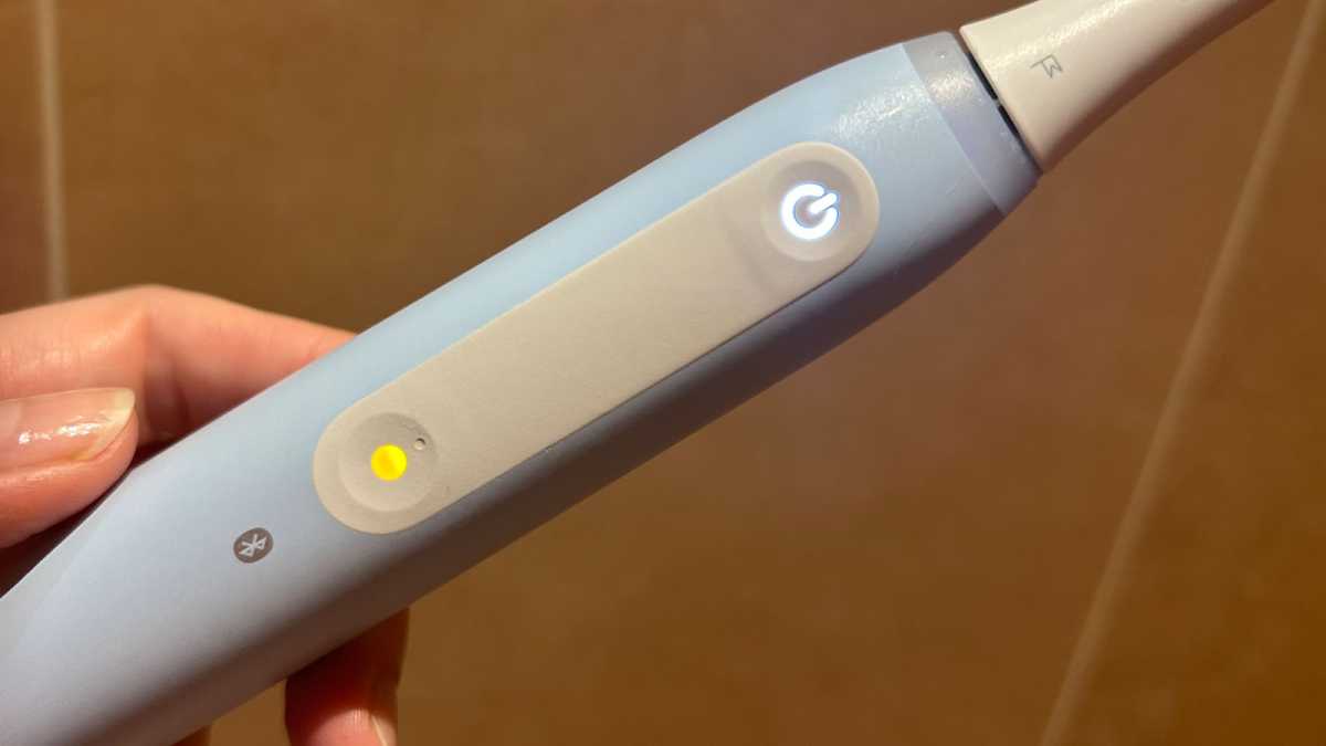 A hand holding an Oral-B brush with a glowing mode button