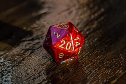 Close-up image of a marbled red 20 sided die on a wet wooden surface outside in the sunlight.